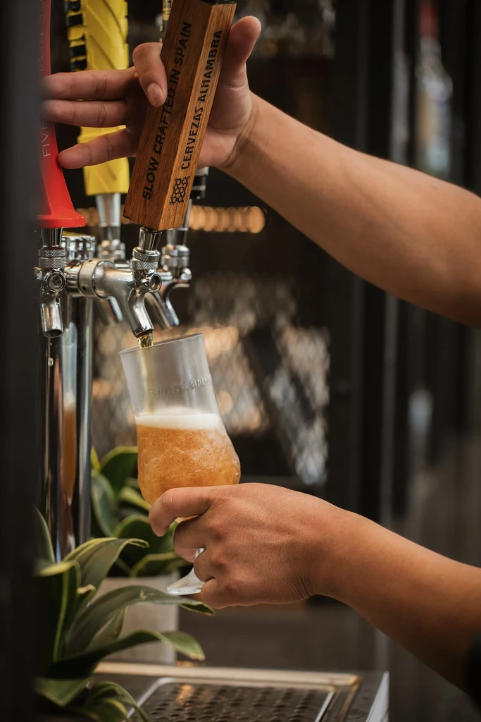 Hands pour Cervezas Alhambra beer from a tap into a glass.