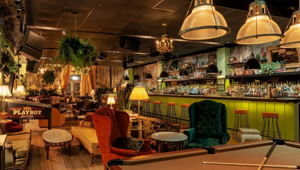 Dimly lit, eclectic bar with pool table, pinball, and vintage lounge furniture.