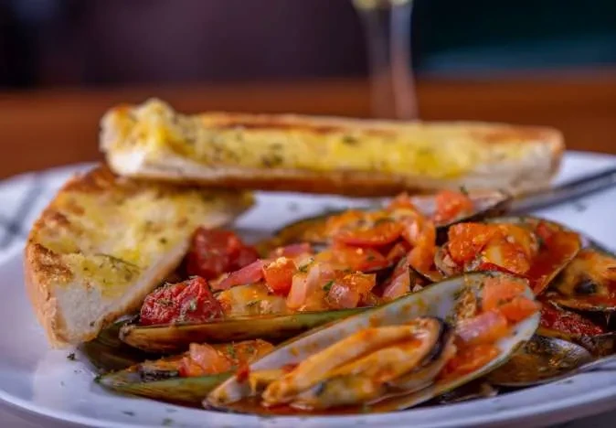 Plate of mussels with tomato sauce, herbs, and golden-brown garlic bread.