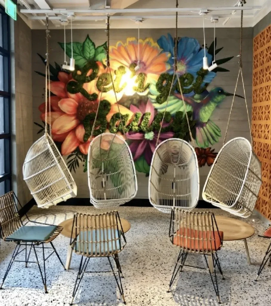 Colorful flower mural with "Let it Grow" text and modern swing chairs.