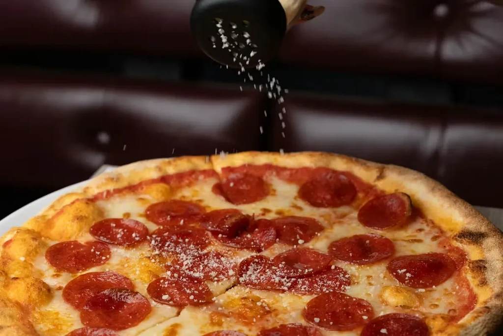 Freshly baked pepperoni pizza with grated cheese being sprinkled on it.