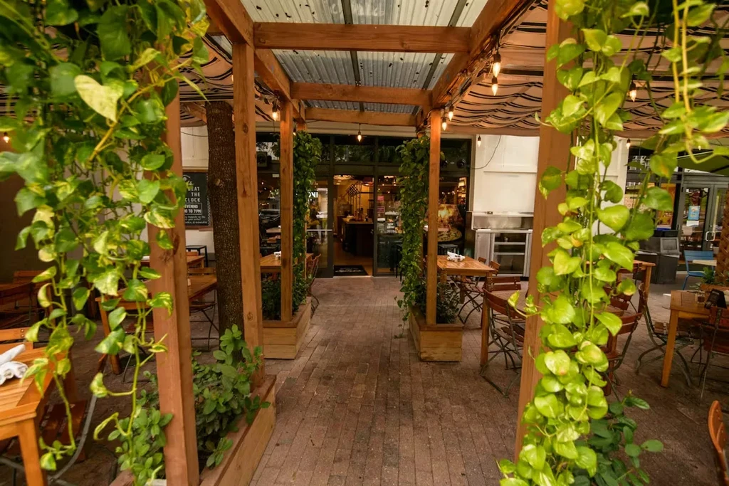 Outdoor restaurant patio with vine-covered pergola and dining tables.