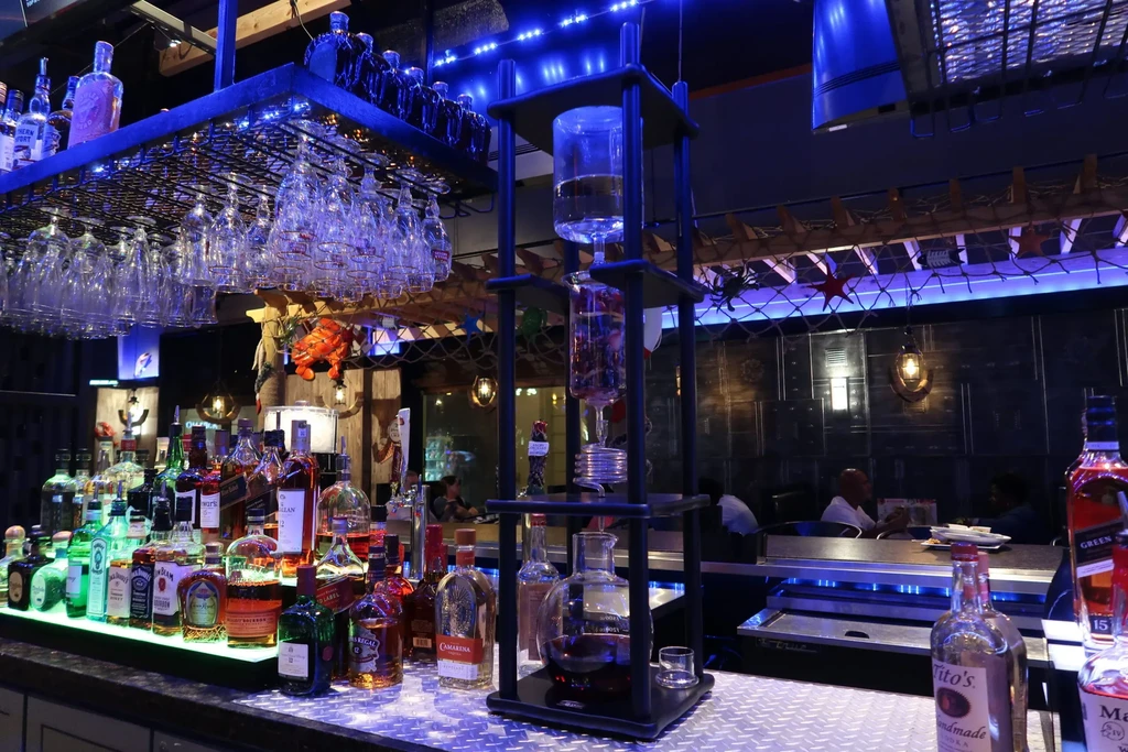 Illuminated bar with liquor bottles, hanging glasses, and blue LED lights.