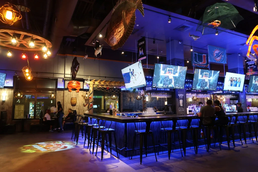 Vibrant sports bar interior with blue-lit bar, TVs, and nautical decor.