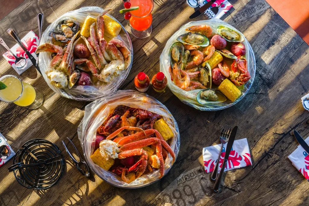 Overhead: Three bags of seafood boil and cocktails on a rustic table.