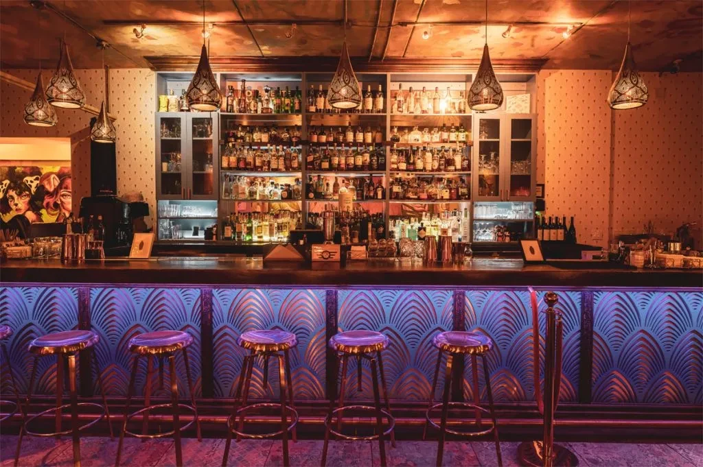 Elegant bar interior with glowing bottles, art deco facade, and empty stools.
