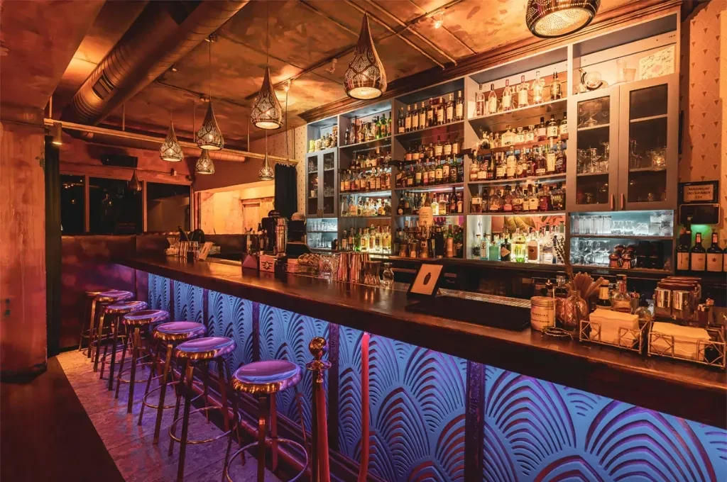 Empty, stylish bar with a purple-lit counter and warm pendant lights.