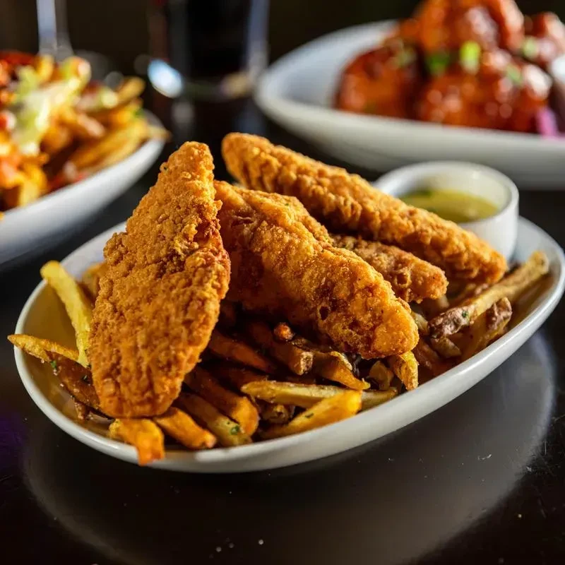 White plate with crispy golden chicken tenders, fries, and green dipping sauce.