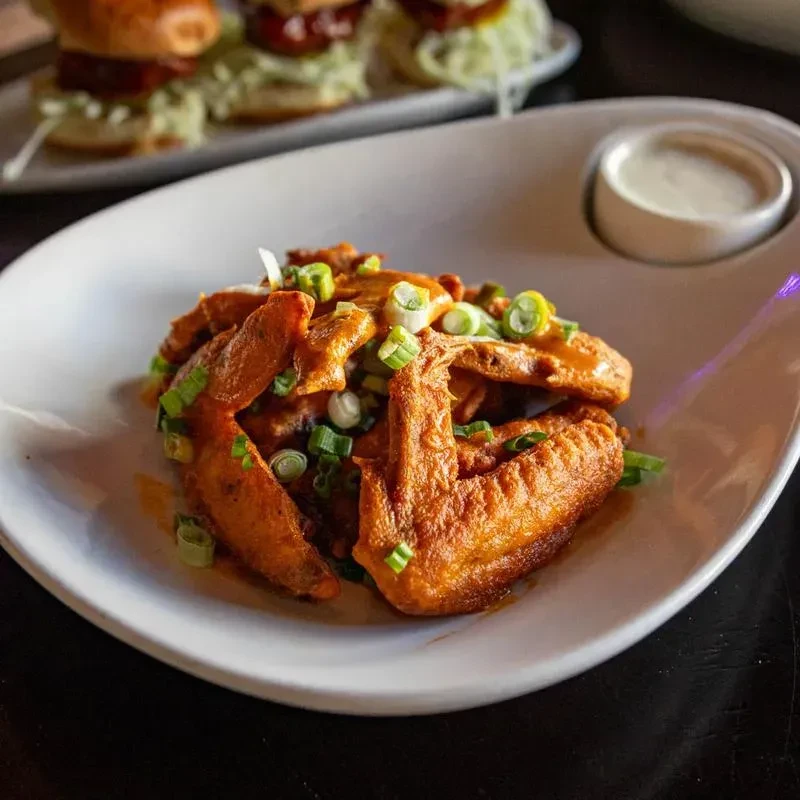 Close-up of saucy chicken wings with green onions and dipping sauce.