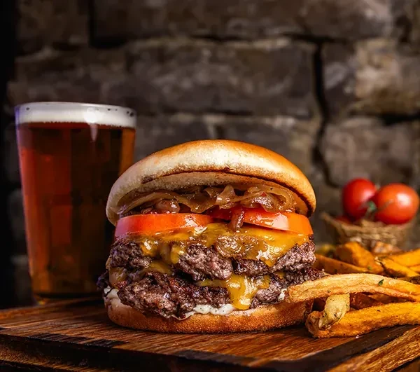 Double-patty cheeseburger with melted cheese, fries, and beer on wooden board.