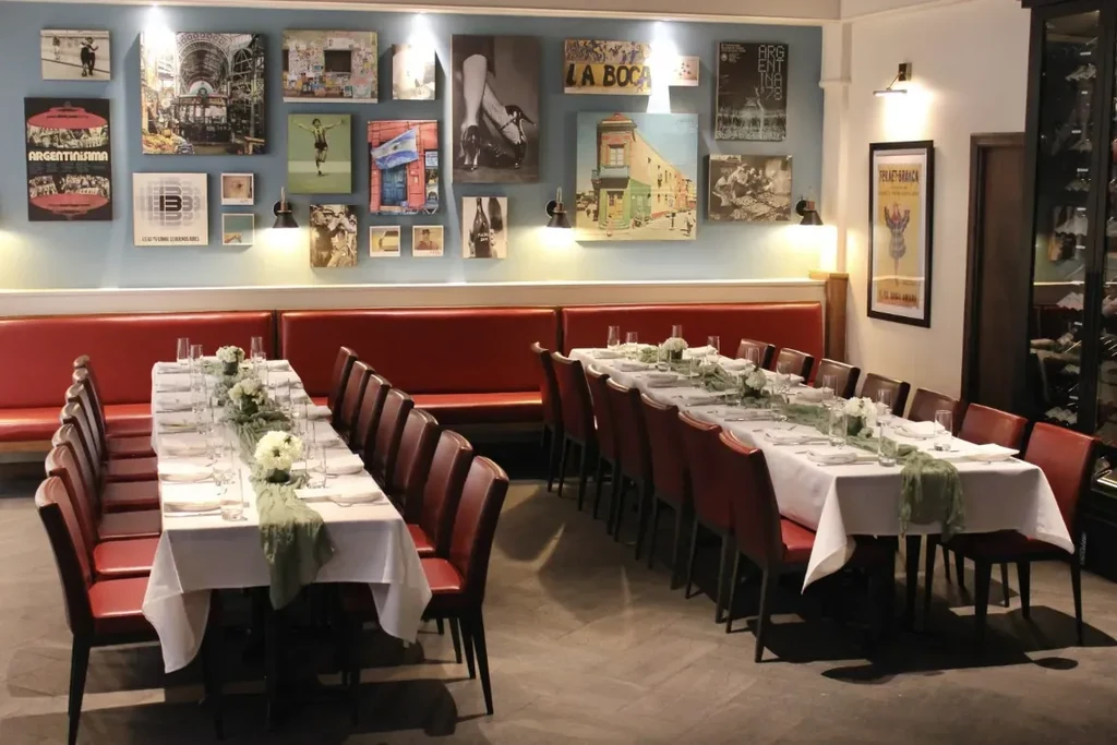 Well-appointed restaurant with long tables, red seating, and Argentine art.