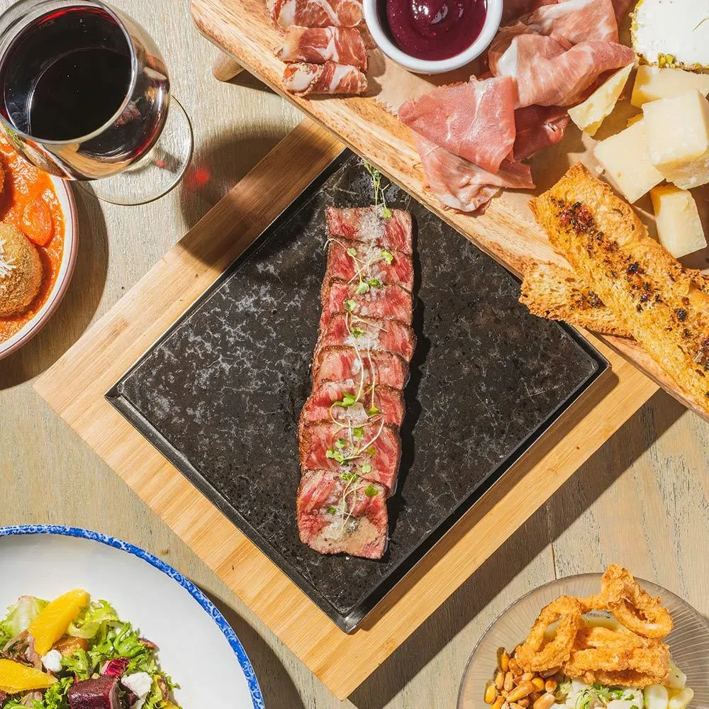Overhead view of sliced beef, charcuterie, wine, salad, and calamari dishes.