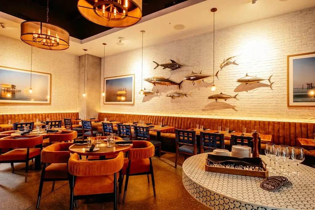 Sophisticated restaurant interior with velvet chairs, brick walls, and fish sculptures.