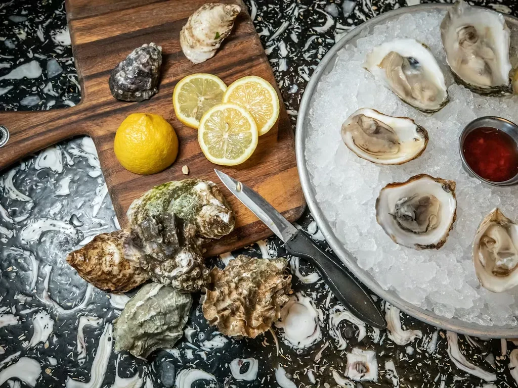 Display of fresh shucked and unshucked oysters, lemons, and dipping sauce.
