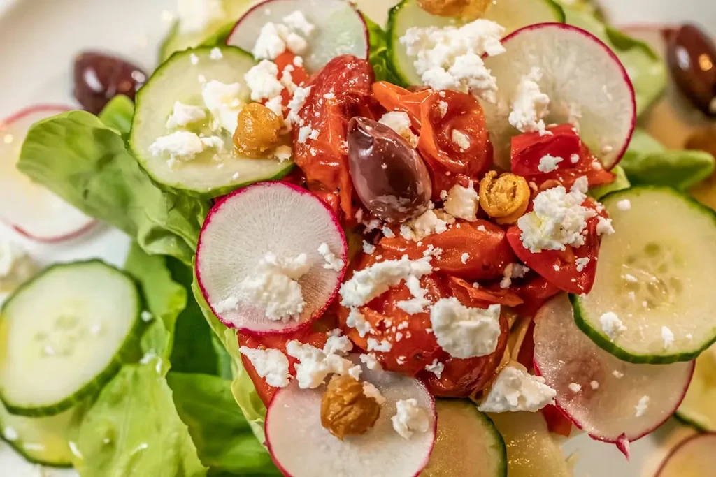 Fresh salad close-up with crisp lettuce, cucumber, radish, tomato, feta, olives.