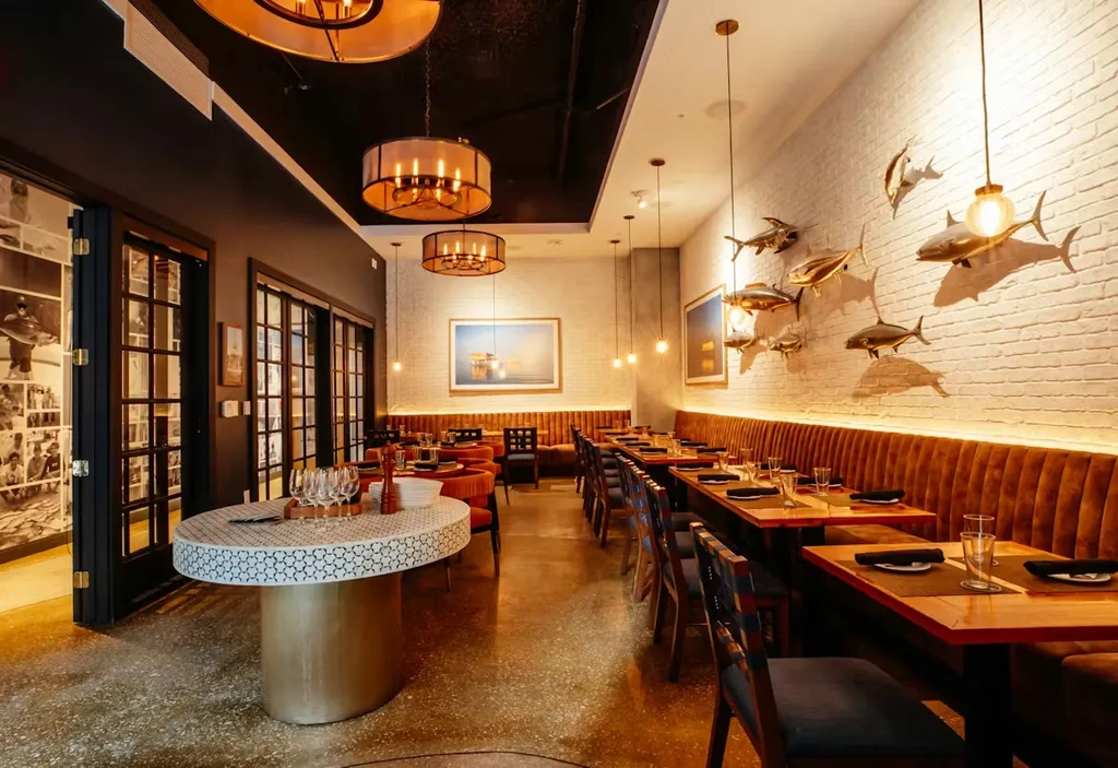Sophisticated restaurant's long dining area with orange booths and metallic fish sculptures.