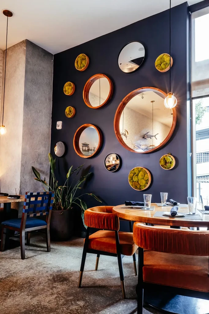 Modern restaurant interior with a mirrored wall and orange velvet chairs.
