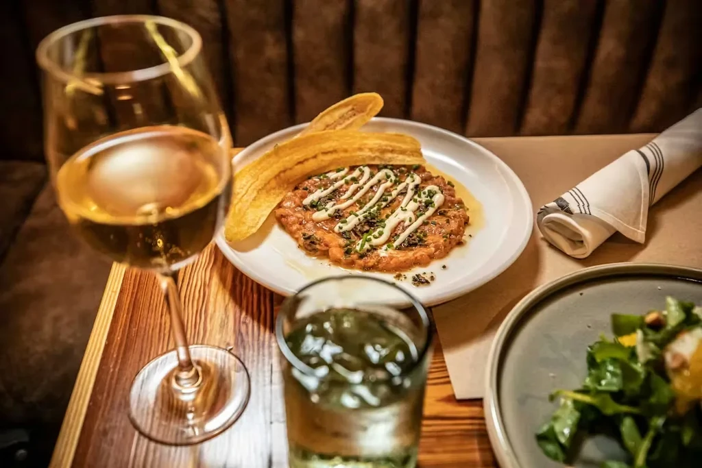 Garnished savory dish with plantain chips and wine on a wooden table.