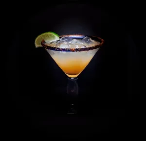 Two-toned cocktail in martini glass with chili-lime rim and lime wedge.