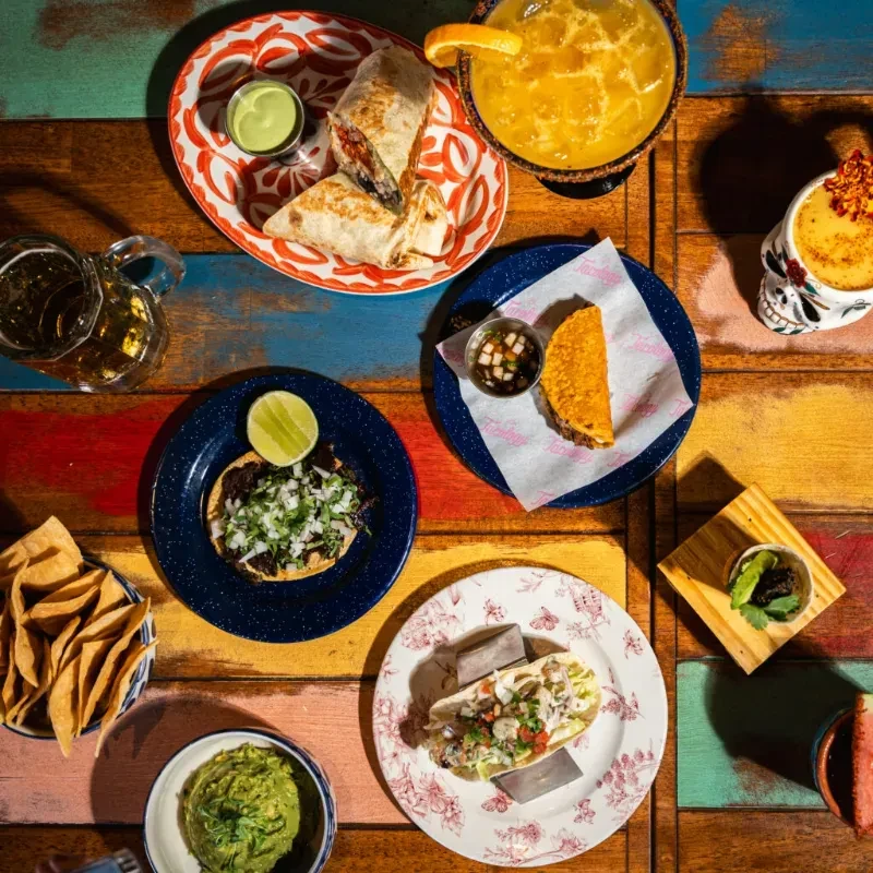 Overhead shot of vibrant Mexican food and drinks on a colorful table.
