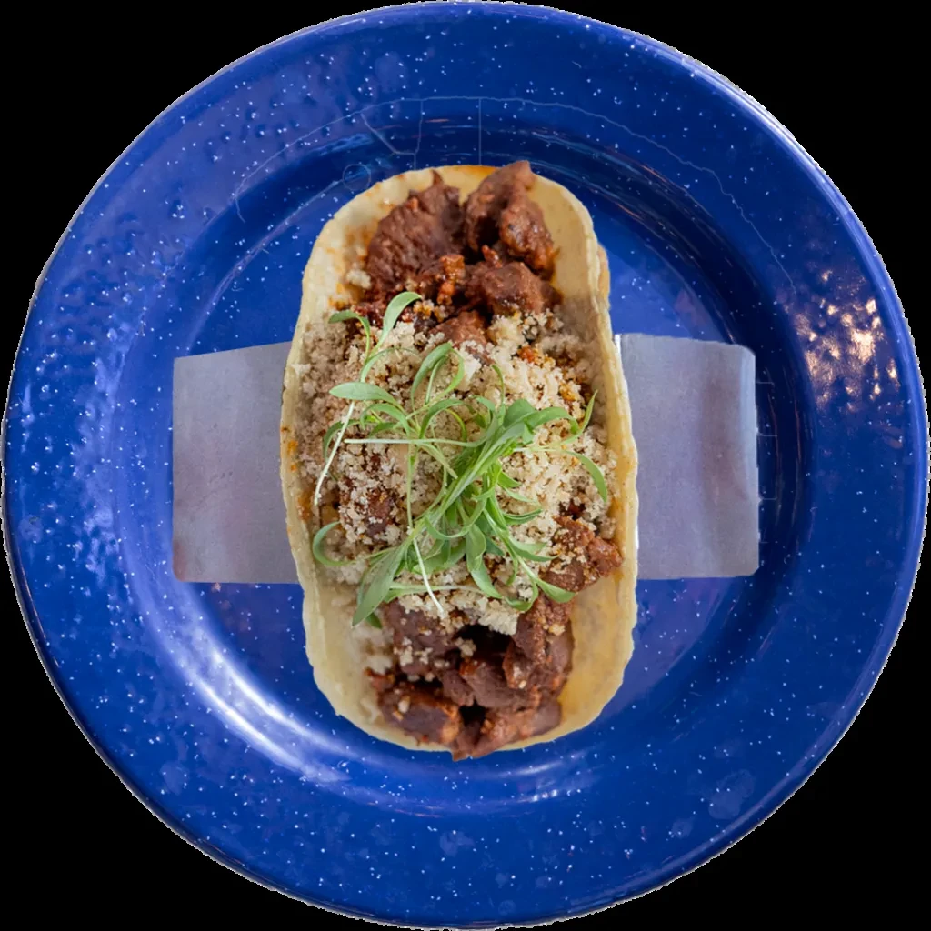Taco with seasoned meat, cheese, and green herbs on a blue plate.