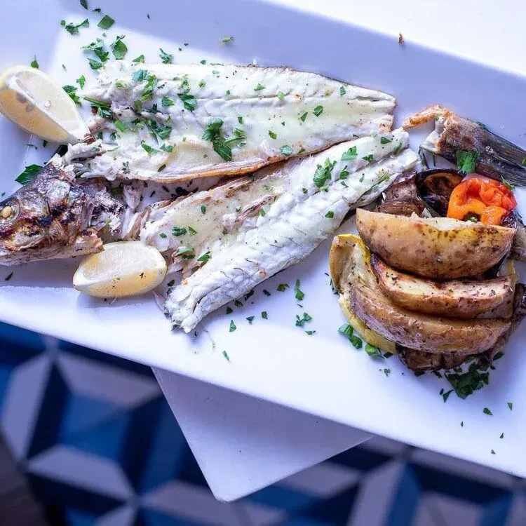 Grilled fish fillets with roasted potatoes, vegetables, and lemon.