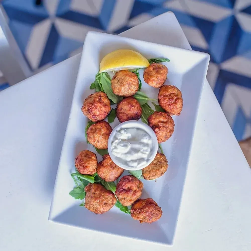 Plate of golden fritters, green leaves, white dipping sauce, and lemon.