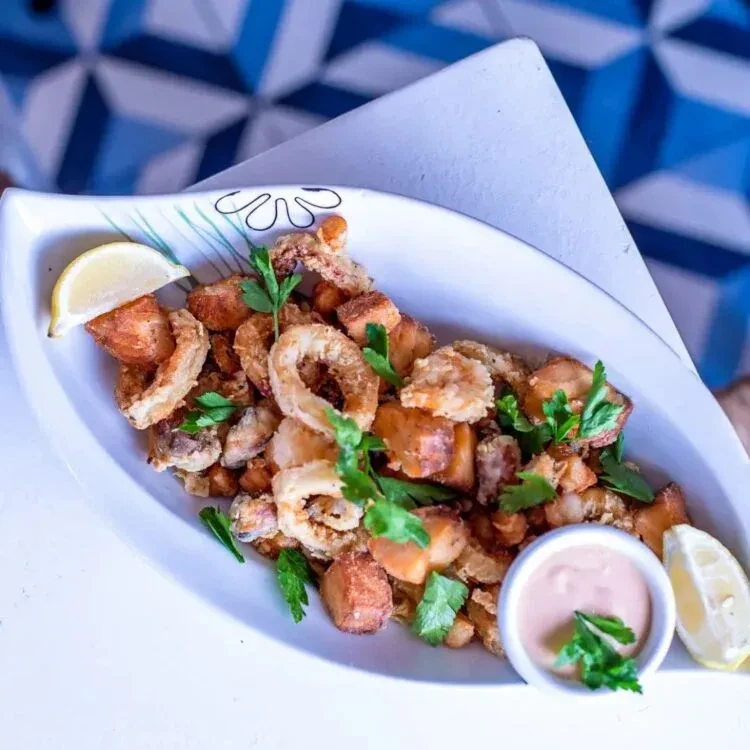Overhead of crispy fried seafood and potatoes with lemon and pink sauce.