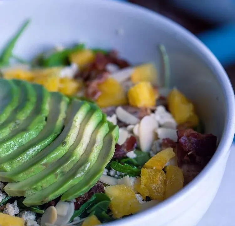 Colorful power bowl with fanned avocado, greens, fruit, and nuts.