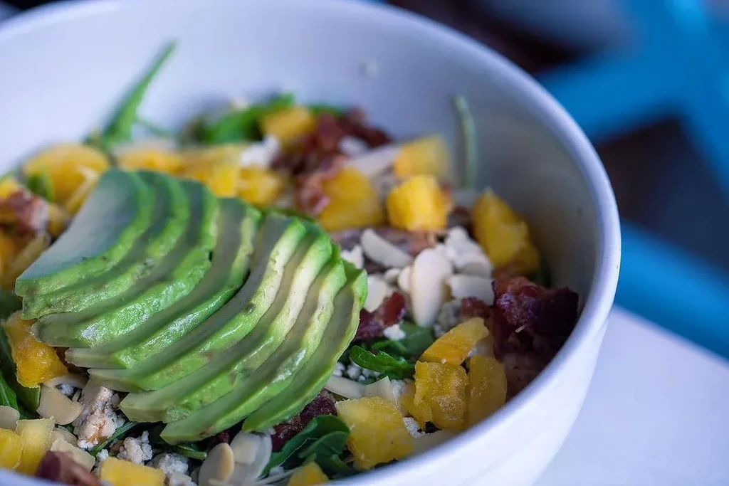 Close-up, top-down vibrant salad in white bowl with fanned avocado.