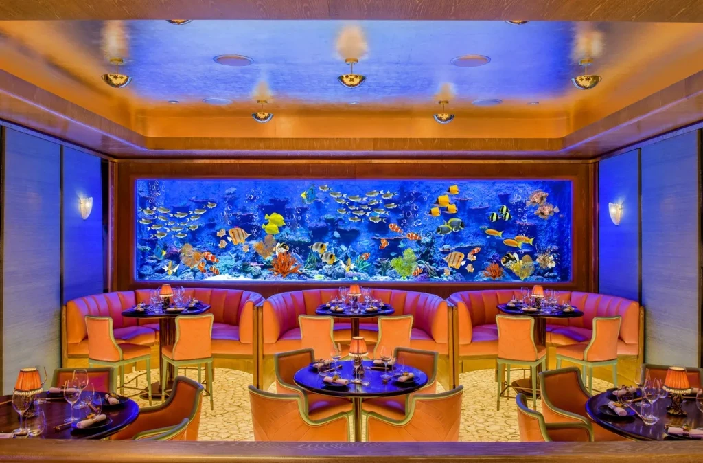 A luxurious restaurant interior with a vibrant full-wall aquarium and orange booths.