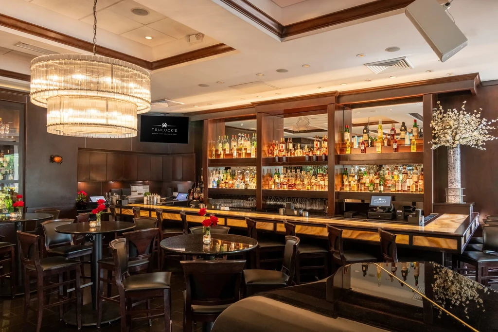 Elegant Truluck's restaurant bar with bottles, piano, and chandelier.