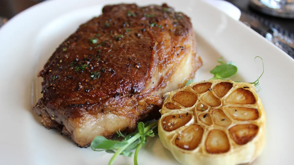 Seared steak, roasted garlic, and green garnish on a white plate.