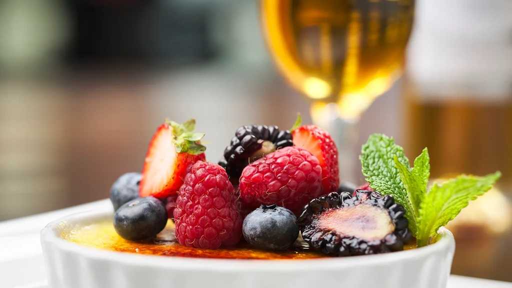Crème brûlée in a white ramekin with caramelized sugar, berries, and mint.