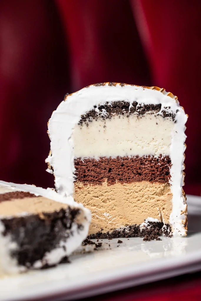 Multi-layered dessert slice on white plate, topped with white frosting.