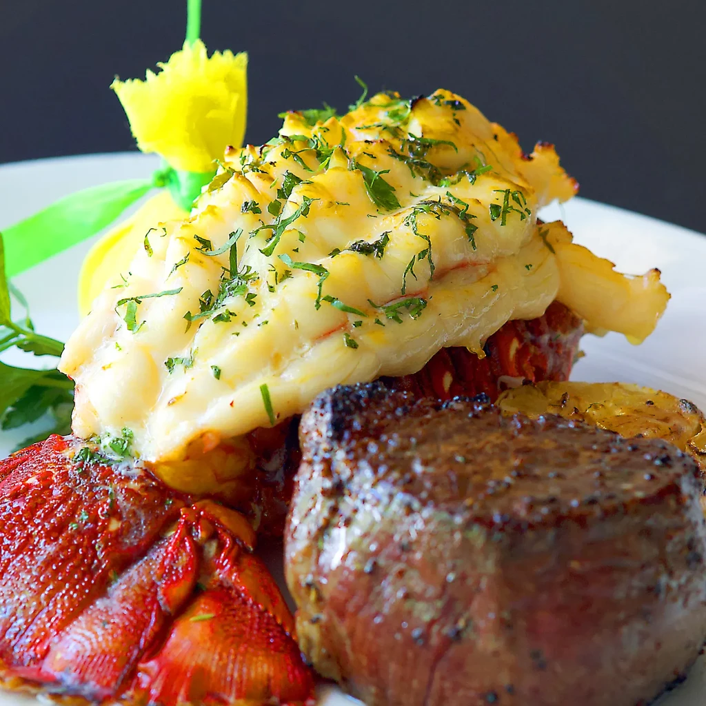 Surf and turf dish featuring lobster tail and seared steak.