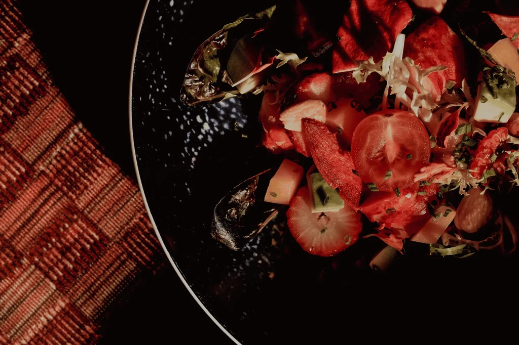 Overhead view of vibrant fruit and vegetable salad in a dark bowl.