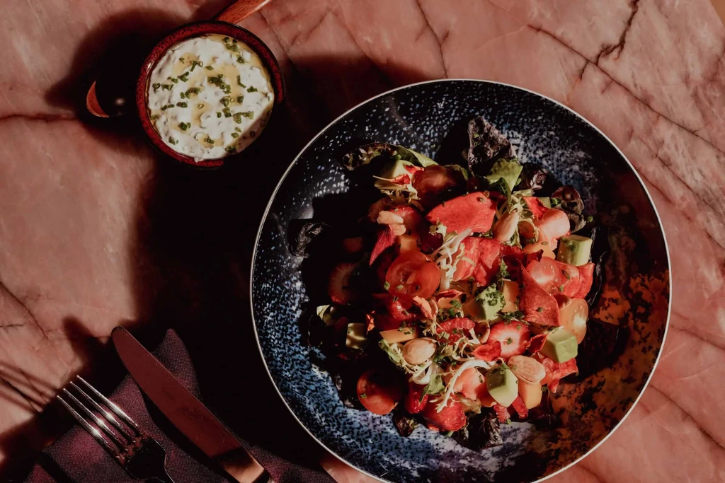 Colorful salad, creamy dip, fork, knife on a marble table.