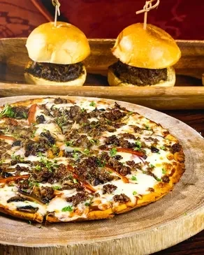 Meat pizza with mushrooms and two sliders on wooden serving boards.