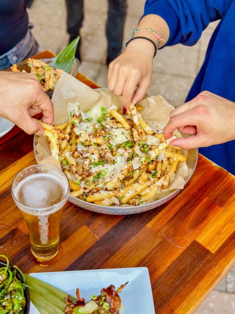 Multiple hands reach for loaded French fries and beer.