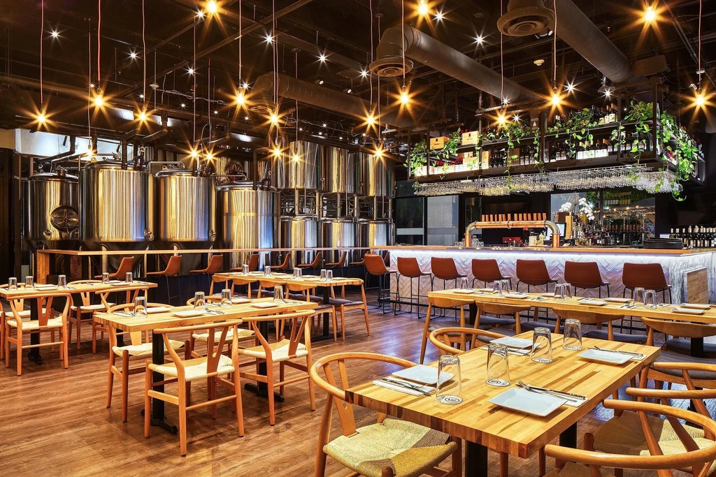 Wide shot of an empty modern brewpub with tanks, tables, and bar.