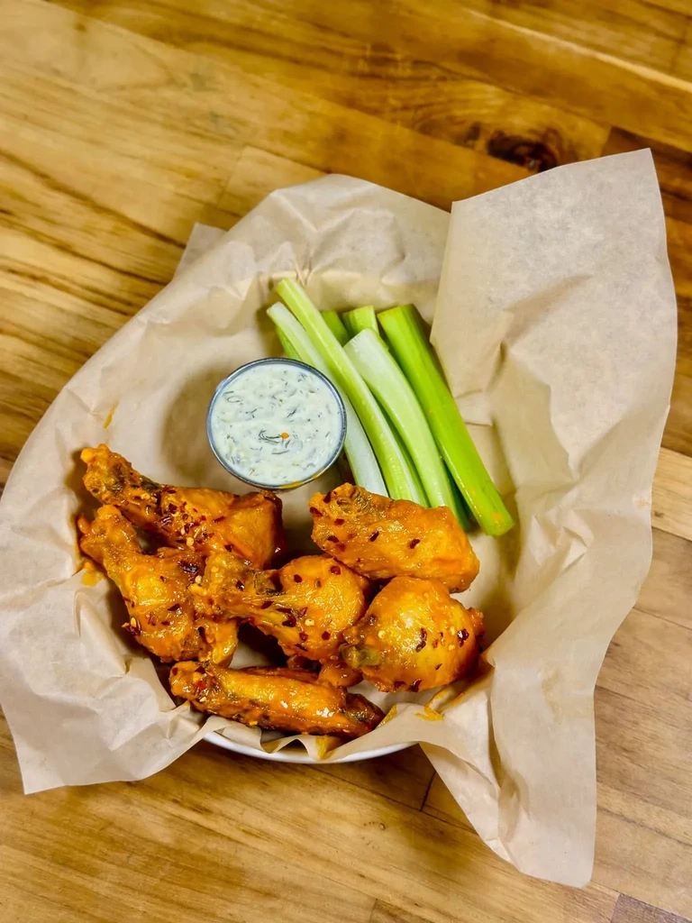 Orange chicken wings, creamy green dip, and fresh celery.