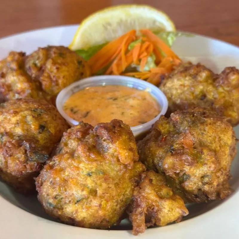 Plate of crispy deep-fried fritters, dipping sauce, lemon, and carrots.