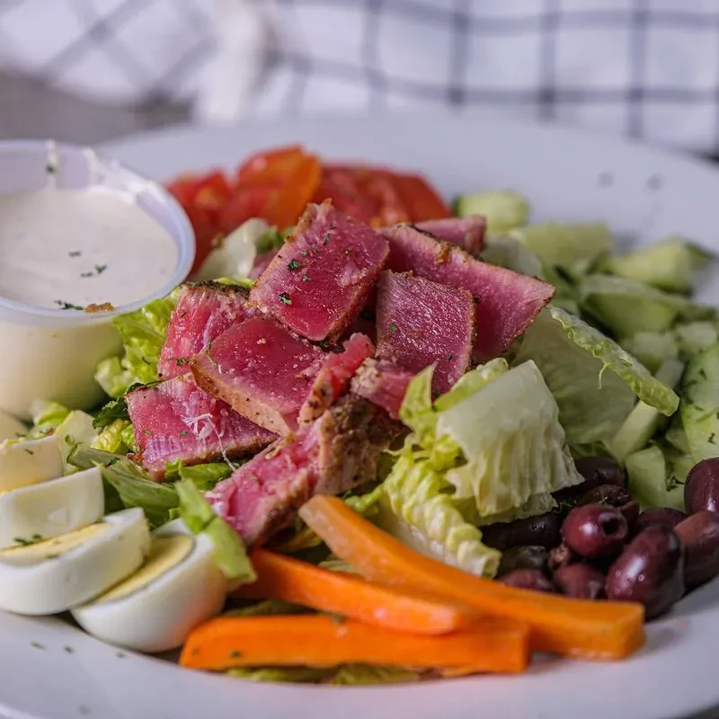 Close-up of seared tuna salad with eggs, olives, carrots, and dressing.