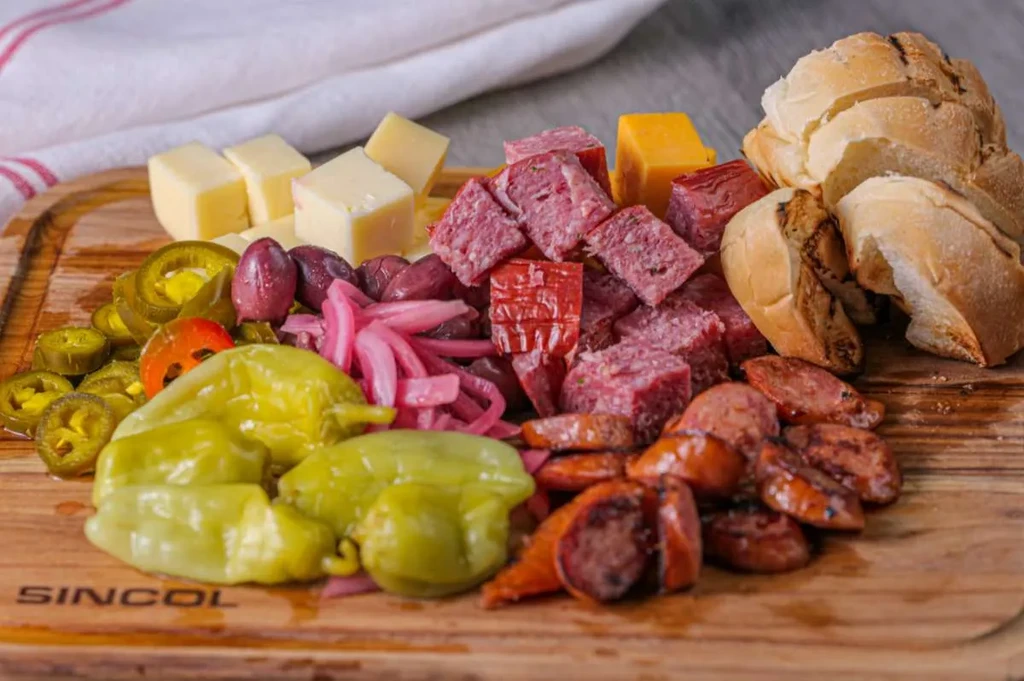 Appetizer board with cheese, cured meats, pickled vegetables, and bread.