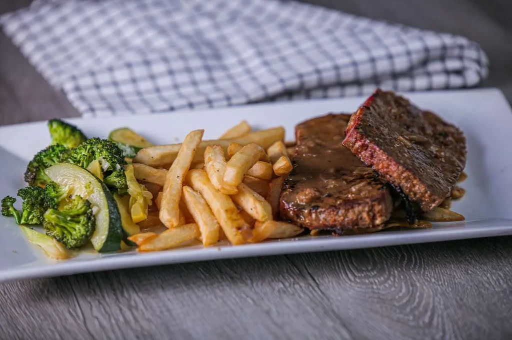 Steak, french fries, broccoli, and zucchini on a white plate.