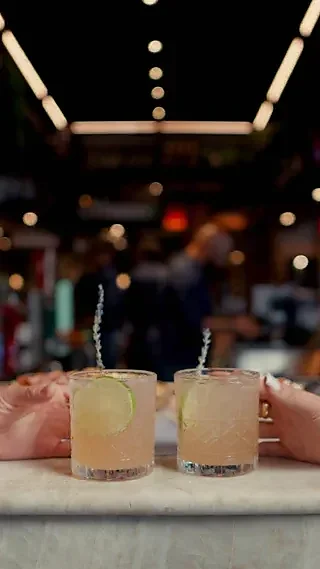 Two citrus cocktails with lime wheels held on marble bar