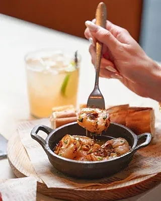 Cast iron skillet of garlic shrimp served with bread and cocktail