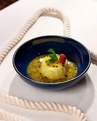 Custard dessert with passion fruit sauce and mint in blue bowl