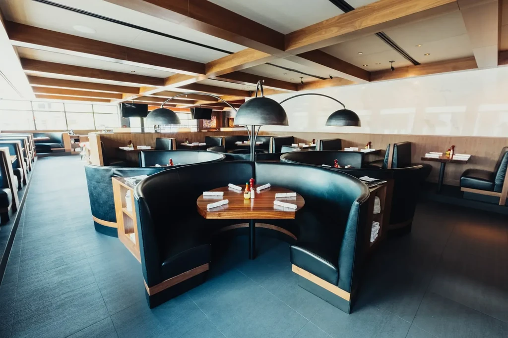 Empty modern restaurant with curving dark booths, wood trim, and arching lights.